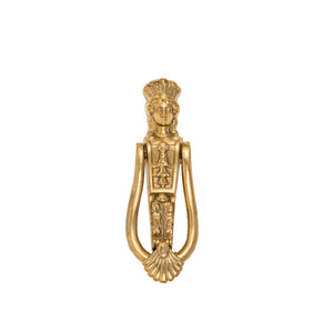 A solid brass door knocker featuring a detailed Caryatid design. The Caryatid is a graceful figure of a woman, inspired by classical architecture, with flowing drapery and elegant features. The knocker ring is positioned below the figure, sturdy and easy to grasp. The polished brass surface gives it a warm, golden glow, adding a touch of timeless beauty to any door.