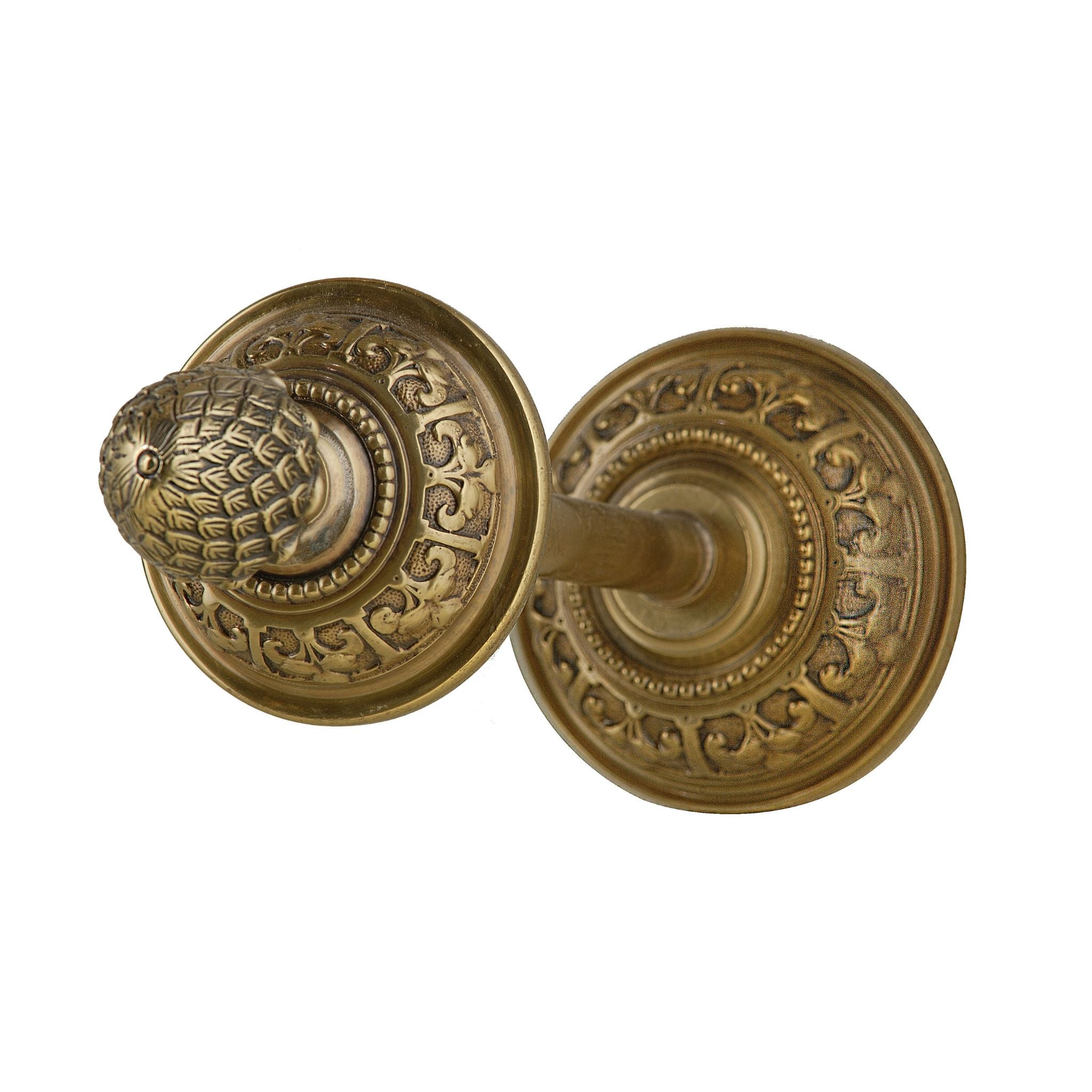 A circular brass tieback featuring a detailed pinecone ornament. The brass surface is smooth and polished, while the pinecone element has textured details that add a touch of nature-inspired elegance. This tieback is sturdy and provides a decorative, refined accent for holding curtains in place.